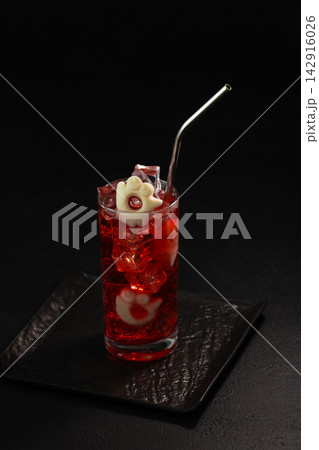 Halloween themed red cocktail with ice and garnish on black background served in a glass with metal straw Halloween themed red cocktail with ice and garnish on black background served in a glass with metal straw 142916026