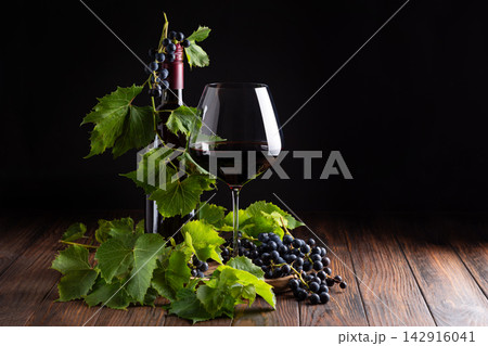 Elegant Red Wine Bottle And Glass With Fresh Grapes And Leaves On Wooden Table 142916041