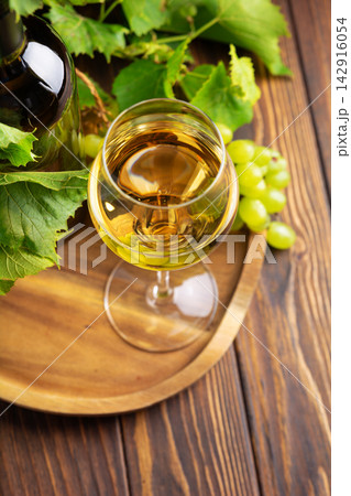 Glass of white wine bottle and green grapes on wooden tray with vine leaves 142916054