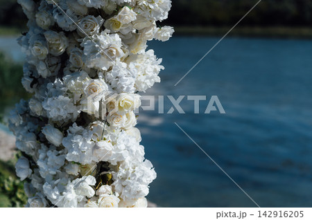 White rose floral arch detail for outdoor wedding ceremony by the lake. White rose floral arch detail for outdoor wedding ceremony by the lake. 142916205