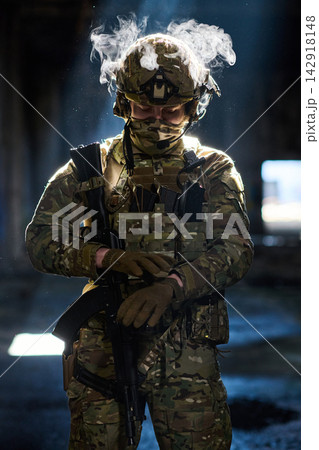 Armed Soldier In Tactical Camouflage Gear With Helmet And Rifle Standing In Dim Urban Environment Armed Soldier In Tactical Camouflage Gear With Helmet And Rifle Standing In Dim Urban Environment 142918148