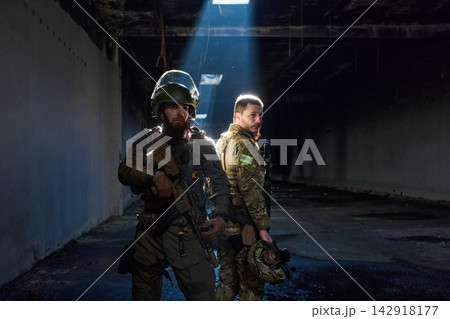 Two Soldiers in Tactical Gear Standing Back-to-Back in Dark Urban Military Interior Two Soldiers in Tactical Gear Standing Back-to-Back in Dark Urban Military Interior 142918177