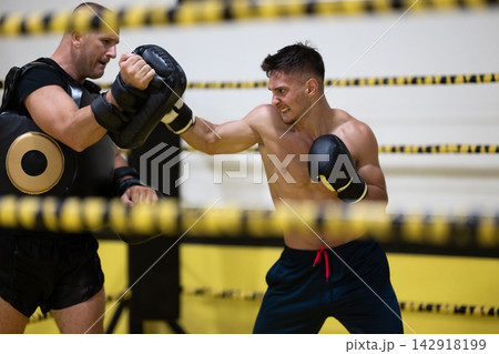 Young Boxer Sparring With Trainer Using Punch Pads In Boxing Gym Training Session Young Boxer Sparring With Trainer Using Punch Pads In Boxing Gym Training Session 142918199
