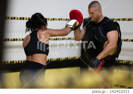 Female Boxer Training With Coach Holding Focus Mitts In A Boxing Ring During Intense Workout Session 142918331