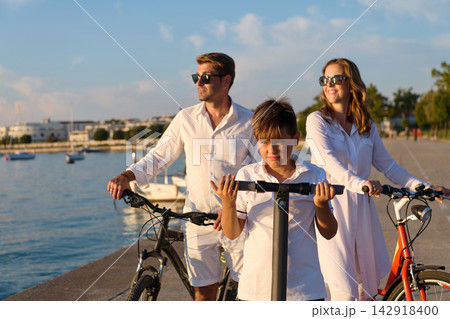 Family Biking and Scooter Ride Along Seaside Promenade at Sunset Parents and Son Together Family Biking and Scooter Ride Along Seaside Promenade at Sunset Parents and Son Together 142918400