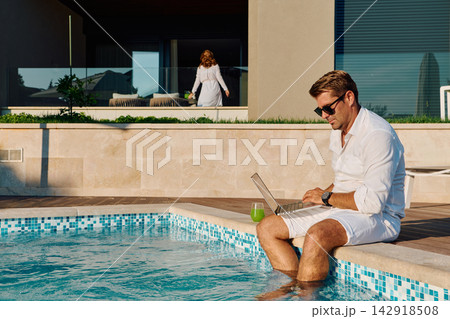 Man Working on Laptop by Poolside in Luxury Vacation Home Summer Remote Work and Relaxation Man Working on Laptop by Poolside in Luxury Vacation Home Summer Remote Work and Relaxation 142918508