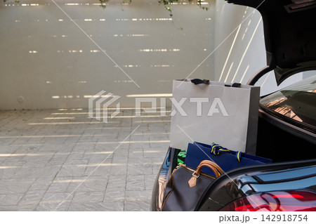 Shopping Bags and Luggage in an Open Car Trunk on a Sunny Driveway Ready for Travel Shopping Bags and Luggage in an Open Car Trunk on a Sunny Driveway Ready for Travel 142918754
