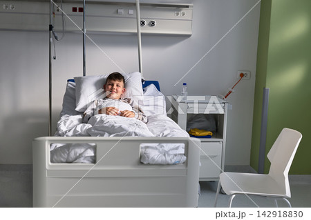 Smiling child resting in a hospital bed during a calm afternoon in a pediatric ward 142918830