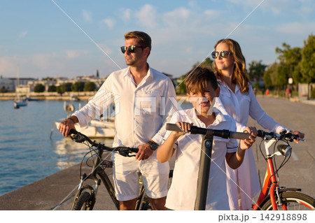 Family Riding Bicycles and Electric Scooter Along Waterfront Promenade at Golden Hour Family Riding Bicycles and Electric Scooter Along Waterfront Promenade at Golden Hour 142918898