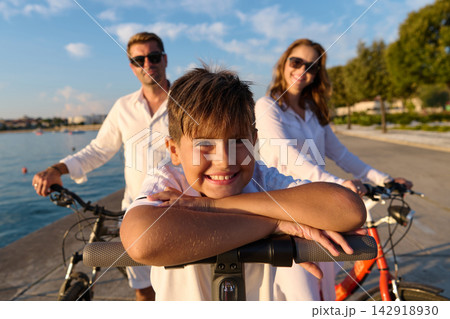 Happy Family With Smiling Boy on Bikes Enjoying Summer Seaside Ride at Sunset Happy Family With Smiling Boy on Bikes Enjoying Summer Seaside Ride at Sunset 142918930