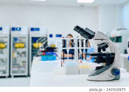 Laboratory scene with microscope and researchers working at medical facility during the day Laboratory scene with microscope and researchers working at medical facility during the day 142918975