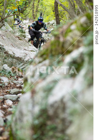 Mountain biker riding a rocky forest trail with helmet camera and protective gear 142918995