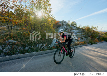 Female Cyclist Training on Scenic Road at Sunrise on Autumn Hillside 142919063