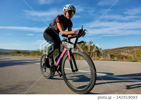 Female Cyclist Riding Road Bike On Open Country Road During Outdoor Training Session Female Cyclist Riding Road Bike On Open Country Road During Outdoor Training Session 142919093