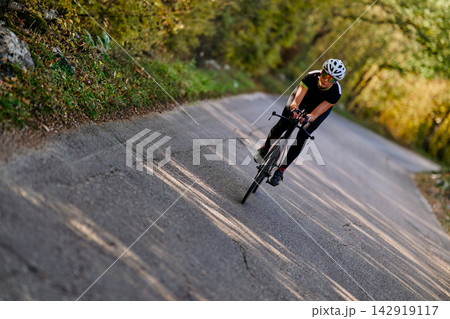 Solo Cyclist Riding Road Bike Through Sunlit Forested Country Road During Outdoor Training 142919117