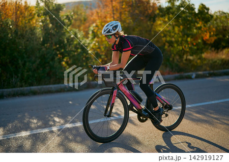 Female Cyclist Training on Road Bike at Sunset Endurance Cycling Athlete in Autumn Landscape 142919127