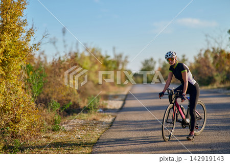 Female Cyclist Riding Road Bike On Quiet Country Road During Sunny Outdoor Training Session Female Cyclist Riding Road Bike On Quiet Country Road During Sunny Outdoor Training Session 142919143