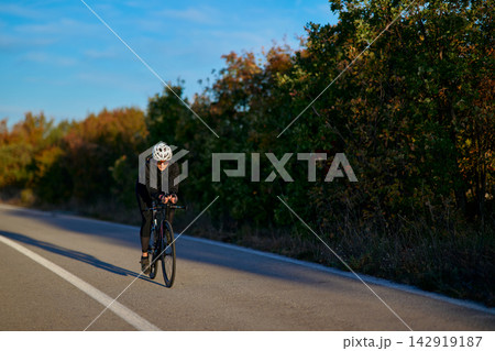 Solo Cyclist Training on a Quiet Country Road at Sunrise Wearing Helmet and Cycling Kit Solo Cyclist Training on a Quiet Country Road at Sunrise Wearing Helmet and Cycling Kit 142919187