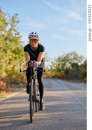 Female Cyclist Training On Quiet Country Road With Aero Bike And Cycling Gear At Sunrise Female Cyclist Training On Quiet Country Road With Aero Bike And Cycling Gear At Sunrise 142919231