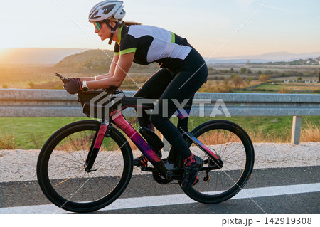 Female Cyclist Training on Road Bike at Sunrise Triathlon Athlete Cycling Workout Outdoors Female Cyclist Training on Road Bike at Sunrise Triathlon Athlete Cycling Workout Outdoors 142919308