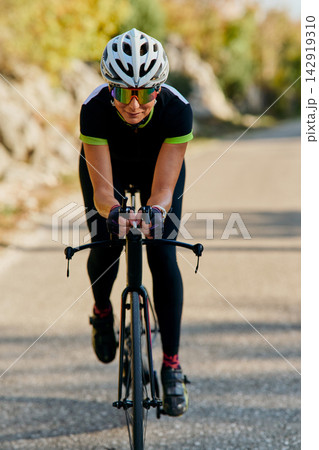 Female Cyclist Riding Road Bike in Aerodynamic Position on Rural Road Training for Speed Female Cyclist Riding Road Bike in Aerodynamic Position on Rural Road Training for Speed 142919310