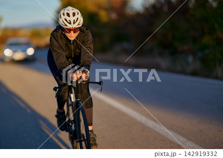 Road Cyclist Riding Fast on Country Road at Sunset Wearing Helmet and Cycling Gear Road Cyclist Riding Fast on Country Road at Sunset Wearing Helmet and Cycling Gear 142919332