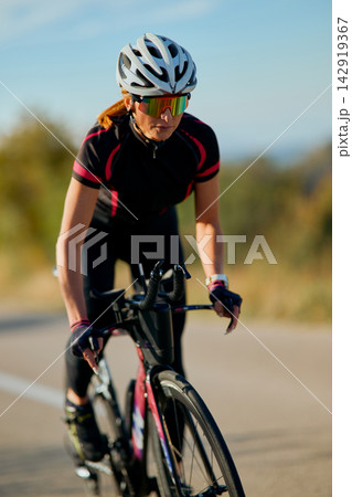 Female Road Cyclist Training on Bicycle in Sunny Outdoor Setting Wearing Helmet and Sunglasses Female Road Cyclist Training on Bicycle in Sunny Outdoor Setting Wearing Helmet and Sunglasses 142919367