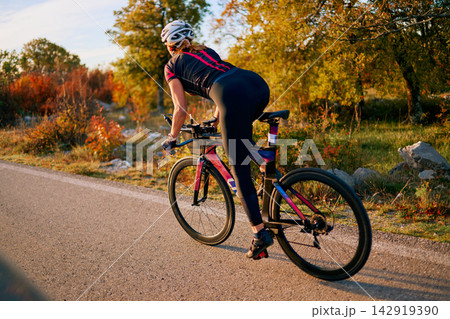 Female Cyclist Training on Road Bike Through Autumn Countryside at Sunset for Fitness Female Cyclist Training on Road Bike Through Autumn Countryside at Sunset for Fitness 142919390