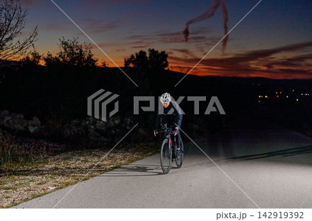 Night Road Cyclist Training At Sunset Wearing Helmet And Reflective Gear On Empty Country Road Night Road Cyclist Training At Sunset Wearing Helmet And Reflective Gear On Empty Country Road 142919392