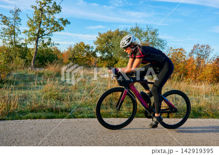 Female Cyclist Training on Road Bike in Autumn Countryside for Fitness and Triathlon Preparation 142919395