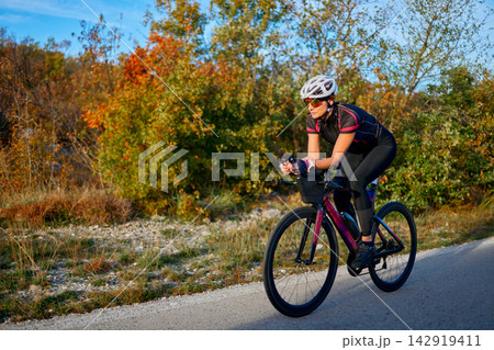 Female Cyclist Training on Road Bike Through Autumn Countryside Wearing Helmet and Cycling Gear 142919411