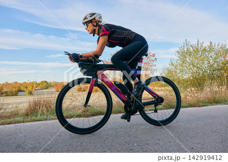 Female Cyclist Riding Aerodynamic Road Bike Outdoors at Sunrise Training for Triathlon and Fitness Female Cyclist Riding Aerodynamic Road Bike Outdoors at Sunrise Training for Triathlon and Fitness 142919412
