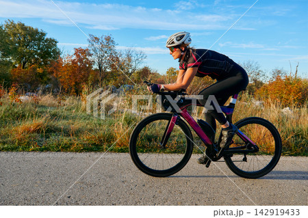 Female Cyclist Riding Aero Road Bike Outdoors at Sunset Training for Fitness and Endurance 142919433