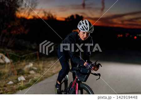Female Cyclist Training on Road at Sunset and Nightfall Wearing Helmet and Cycling Gear Female Cyclist Training on Road at Sunset and Nightfall Wearing Helmet and Cycling Gear 142919448