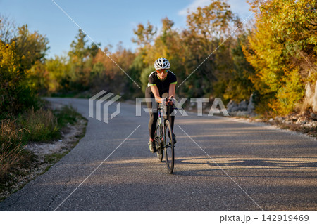 Fit Cyclist Training On Country Road At Sunset Riding A Road Bike For Speed And Endurance 142919469