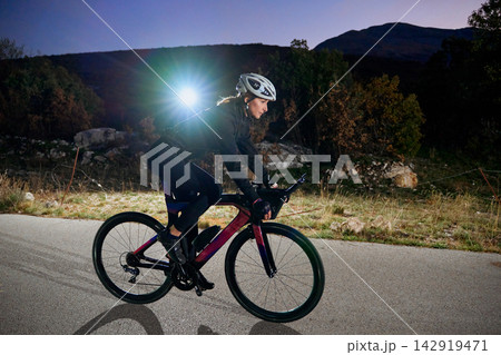 Female Cyclist Training On Road Bike At Dusk With Headlight In Rural Landscape 142919471