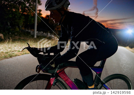 Female Cyclist Training On Road Bike At Dusk With Helmet And Reflective Gear Female Cyclist Training On Road Bike At Dusk With Helmet And Reflective Gear 142919598