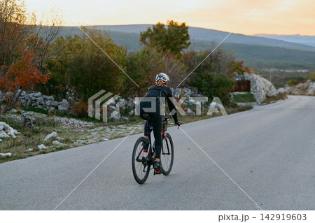 Female Cyclist Riding Road Bike At Sunset Through Countryside For Fitness Training And Scenic Adventure 142919603