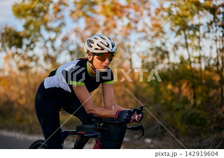 Female Cyclist Training on Road Bike at Sunset, Triathlon Athlete Wearing Helmet and Sunglasses 142919604