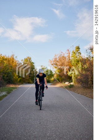 Solo Cyclist Riding Road Bike Through Autumn Countryside for Fitness and Training 142919616