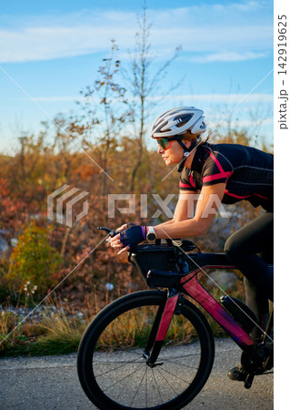 Female Cyclist Training on Aerodynamic Road Bike at Sunset in Autumn Landscape for Fitness 142919625