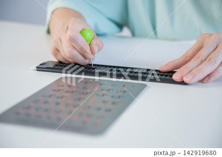A blind woman writes in Braille using a stencil on a piece of paper.  142919680
