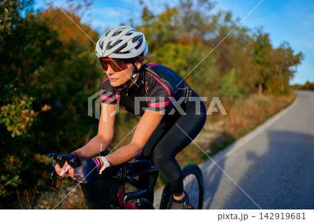 Female Cyclist Training on a Country Road at Sunset Wearing Helmet and Sunglasses Female Cyclist Training on a Country Road at Sunset Wearing Helmet and Sunglasses 142919681