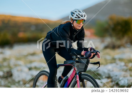 Female Cyclist Training On Road Bike Outdoors Wearing Helmet And Sunglasses In Mountain Landscape Female Cyclist Training On Road Bike Outdoors Wearing Helmet And Sunglasses In Mountain Landscape 142919692
