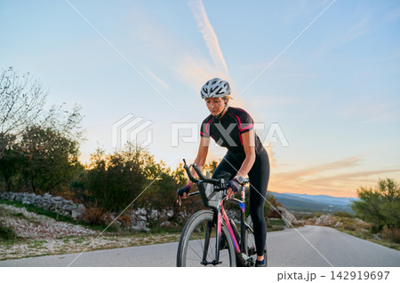Female Cyclist Training On Open Road At Sunset Wearing Helmet And Cycling Gear For Fitness Female Cyclist Training On Open Road At Sunset Wearing Helmet And Cycling Gear For Fitness 142919697