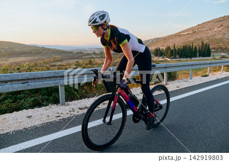 Female Cyclist Training on Road Bike at Sunset With Helmet and Sunglasses in Countryside Female Cyclist Training on Road Bike at Sunset With Helmet and Sunglasses in Countryside 142919803