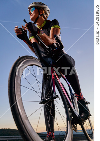 Female Cyclist Riding Road Bike at Sunset With Helmet, Sunglasses and Aero Bars Training Outdoors Female Cyclist Riding Road Bike at Sunset With Helmet, Sunglasses and Aero Bars Training Outdoors 142919835