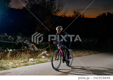 Road Cyclist Training at Dusk on Quiet Country Road Wearing Helmet and Cycling Gear Road Cyclist Training at Dusk on Quiet Country Road Wearing Helmet and Cycling Gear 142919848