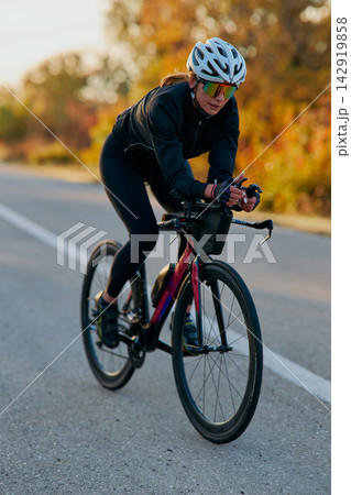 Female Cyclist Training on Road Bike at Sunrise in Autumn Triathlon Time Trial Athlete 142919858