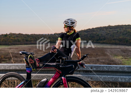 Female Cyclist Resting On Guardrail With Road Bike At Sunset During Outdoor Training Ride Female Cyclist Resting On Guardrail With Road Bike At Sunset During Outdoor Training Ride 142919867